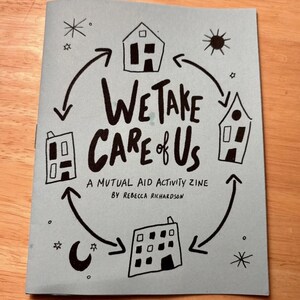 Op de afbeelding: Een lichtblauwe zine met de titel "We Take Care of Us" met zwarte handgeschreven tekst en illustraties van huizen, sterren, een zon en een halve maan. Het is een mutual aid activity zine van Rebecca Richardson.