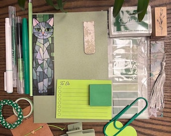 May include: A green and white cat bookmark, a green to-do list notepad, a green heart-shaped sticky note, a green hair clip, a green and white string bracelet, a green and white patterned washi tape, a green and white patterned sticker, a green and white patterned stamp, a green and white patterned paper clip, a green and white patterned envelope, and a green and white patterned pen.