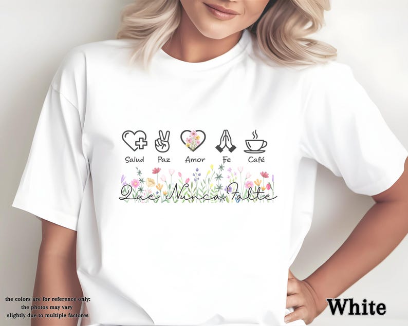 Puede incluir: Camiseta blanca con un dise&ntilde;o gr&aacute;fico que presenta s&iacute;mbolos de salud, paz, amor, fe y caf&eacute;. El dise&ntilde;o incluye elementos florales y el texto "Que Nunca Falte". La camiseta es de cuello redondo.