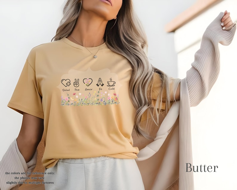Puede incluir: Camiseta color mantequilla con un gr&aacute;fico floral y las palabras "Salud, Paz, Amor, Fe, Caf&eacute;" y "Que Nunca Falte". La camiseta tiene mangas cortas y cuello redondo.