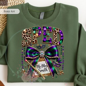 May include: Olive green sweatshirt with a graphic design. The word "SPED" is displayed in leopard print and purple diamond patterns. A large purple and green bow with a pencil and the text "Mr/Mrs Smith" is also featured.