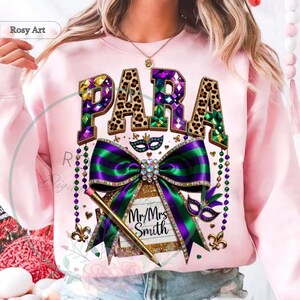 May include: Pink sweatshirt with a colorful Mardi Gras design. The word "PARA" is displayed in a leopard print font with jewel accents. A large green and purple bow is centered below the word, with a pencil and the text "Mr/Mrs Smith".