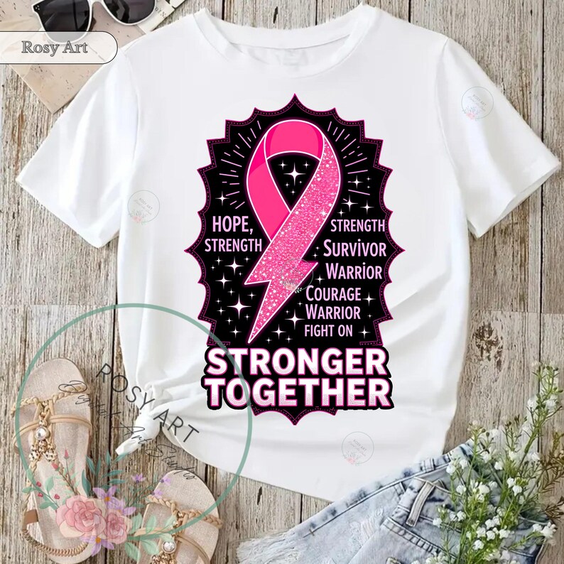 K&ouml;nnte beinhalten: Wei&szlig;es T-Shirt mit einem rosa Schleifendesign und den Worten "HOPE, STRENGTH, SURVIVOR, WARRIOR, COURAGE, FIGHT ON" und "STRONGER TOGETHER". Das Design enth&auml;lt einen rosa Blitz und einen schwarzen Rahmen.