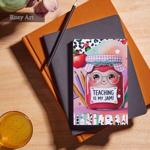 Op de afbeelding: Een notitieboek met een kleurrijke illustratie van een jampot met een bril en de tekst "TEACHING IS MY JAM!". Het notitieboek ligt op een grijs notitieboek en een oranje notitieboek. Een potlood ligt op de notitieboeken.
