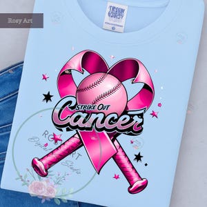 K&ouml;nnte beinhalten: Hellblaues T-Shirt mit einem rosa Baseball, einem rosa Band und gekreuzten rosa Baseballschl&auml;gern. Der Text "Strike Out Cancer" ist in Schwarz und Rosa gehalten. Rosa und schwarze Sterne sind &uuml;ber das Design verstreut.