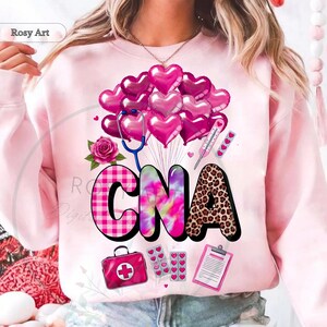 Peut inclure: Sweat-shirt rose clair avec un motif graphique repr&eacute;sentant les lettres "CNA". Le "C" est &agrave; carreaux roses et blancs, le "N" est tie-dye et le "A" est imprim&eacute; l&eacute;opard. Le motif comprend des ballons en forme de c&oelig;ur, un st&eacute;thoscope et des ic&ocirc;nes m&eacute;dicales.