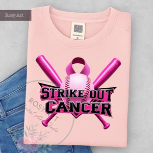 K&ouml;nnte beinhalten: Hellrosa T-Shirt mit Baseball-Design. Es zeigt ein rosa Band, einen Baseball und Schl&auml;ger, mit dem Text "Strike Out Cancer" in Schwarz und Rosa. Das T-Shirt hat einen Rundhalsausschnitt.