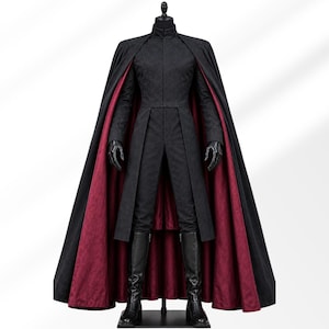 May include: A black long-sleeved tunic with a high collar and a matching floor-length cape featuring a deep red interior lining. The ensemble includes fitted black trousers, black gloves, and black knee-high boots displayed on a mannequin.