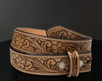 May include: A light brown leather belt with a floral embossed design. The belt features a detailed pattern of flowers and leaves, with a silver buckle and a stitched border. The belt is likely 1.5 inches wide.