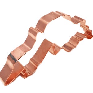 Peut inclure: Un emporte-pièce en métal de couleur cuivre en forme de silhouette animale stylisée. L'objet présente une bande métallique continue et pliée avec une finition métallique réfléchissante et un contour irrégulier formant une créature.