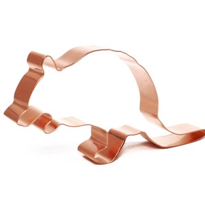 May include: A copper-colored cookie cutter in the shape of a rat. The cutter is made of a single piece of metal, with a simple outline of the animal's body. The rat is depicted in a side profile, with its tail curved.
