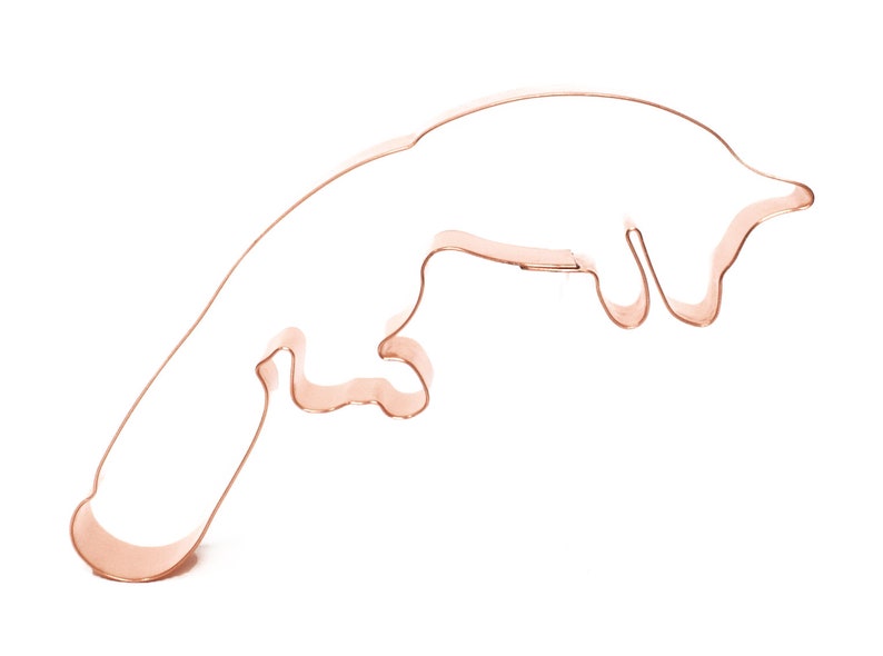 May include: A copper cookie cutter shaped like a jumping otter. The otter is in mid-air with its legs extended and its tail curled.