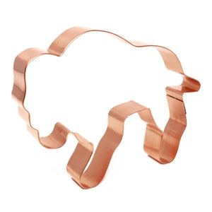 May include: A copper-colored metal cookie cutter shaped like a buffalo. The cutter has a detailed design with a wavy outline.