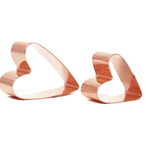 May include: Two copper heart-shaped cookie cutters, one larger than the other, isolated on a white background.