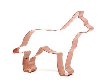 May include: Copper cookie cutter in the shape of a dog. The cutter is a silhouette of a dog standing with its legs spread apart.