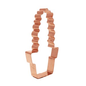 Może przedstawiać: Ciastko wykrawacz w kolorze miedzi w kształcie kaktusa z falistym, fakturowanym wzorem. Wykrawacz ma około 7,5 cm wysokości.