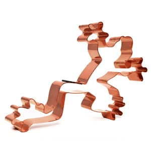 May include: A copper cookie cutter shaped like a reindeer with a raised design. The reindeer is standing on its hind legs with its front legs outstretched.