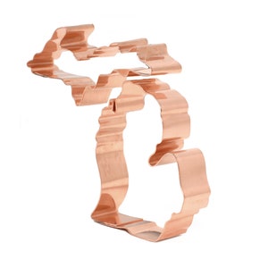 May include: A copper-colored cookie cutter in the shape of the state of Michigan. The cutter has a wavy edge and is designed to cut out cookies.