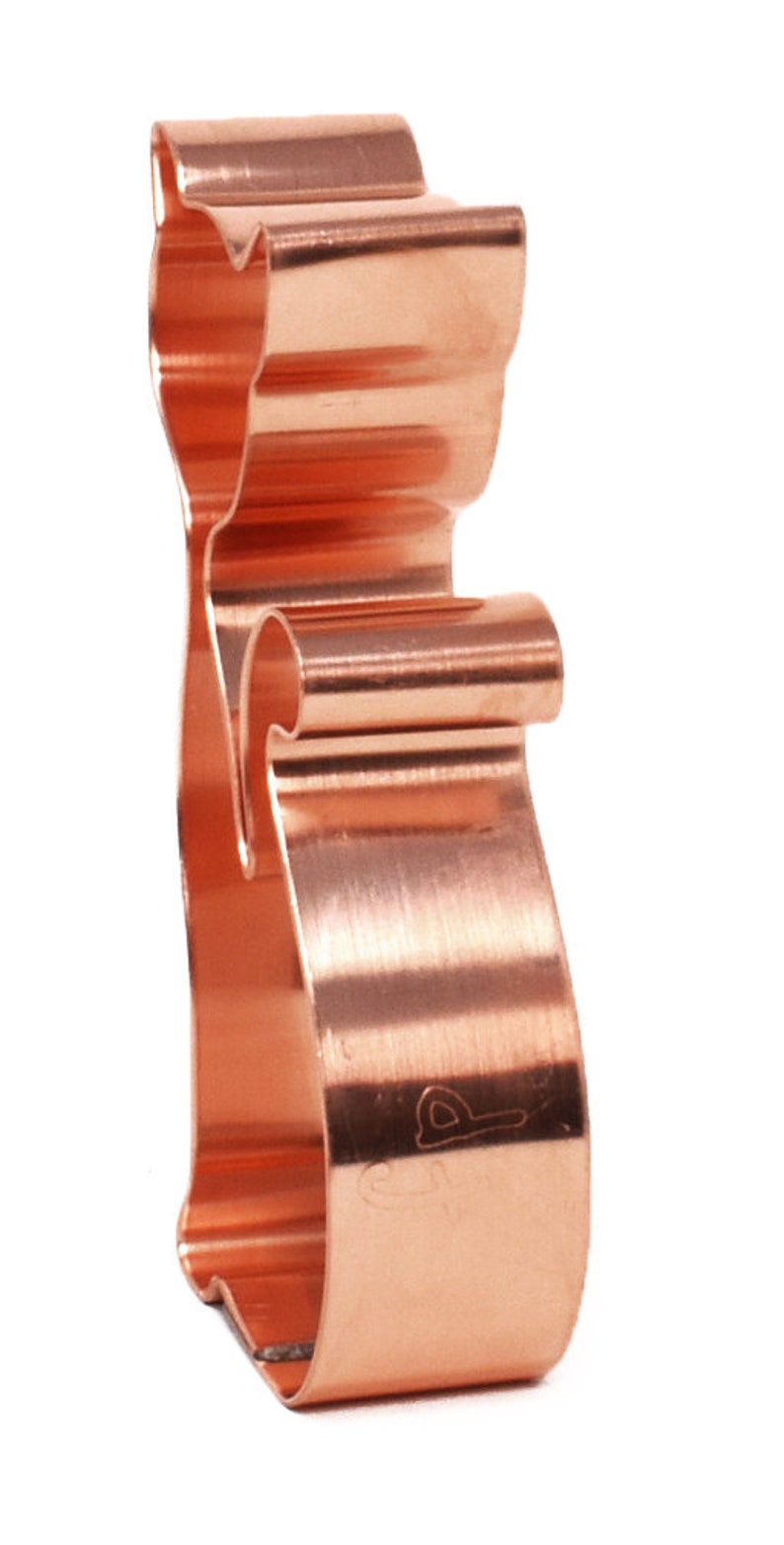 May include: A copper-colored cookie cutter shaped like a cat. The cutter is made of metal and has a smooth, polished finish.
