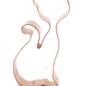 May include: A copper-colored metal cookie cutter shaped like a cat sitting with its tail curled around its legs.
