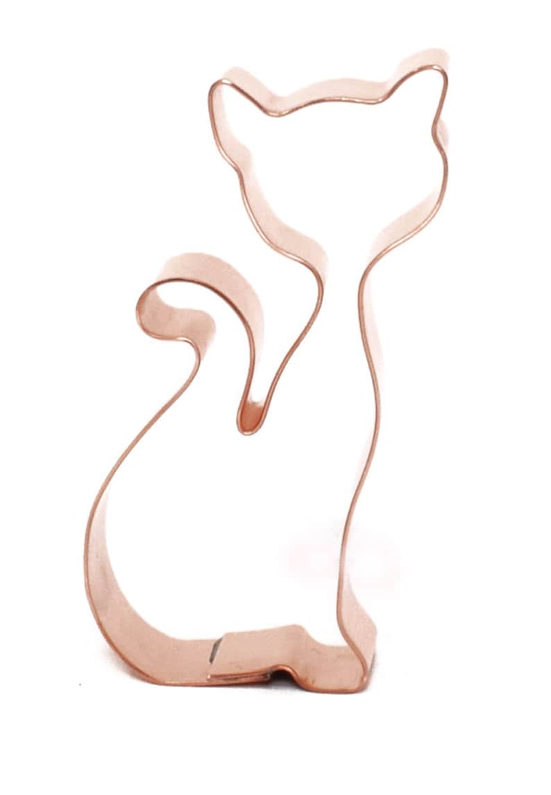 May include: A copper-colored metal cookie cutter shaped like a cat sitting with its tail curled around its legs.
