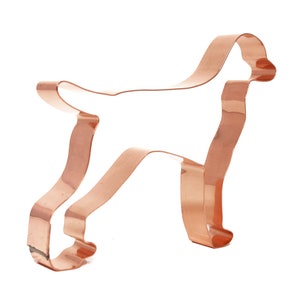 May include: Copper cookie cutter in the shape of a dog. The cutter is standing on a white surface.