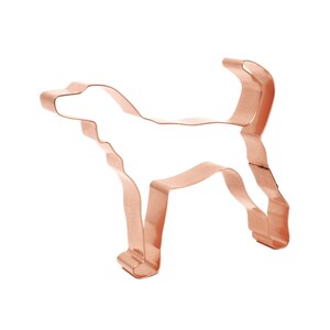 May include: A copper-colored metal cookie cutter in the shape of a dog. The dog is standing with its tail curled up.
