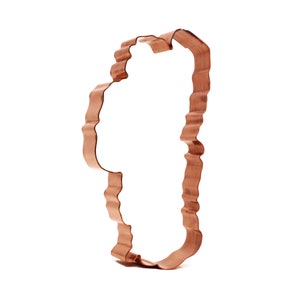 May include: A copper-colored metal cookie cutter shaped like a Christmas tree. The cutter has a scalloped edge and a wavy design.