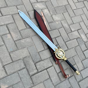 Puede incluir: Una espada decorativa con una hoja azul claro y una empu&ntilde;adura dorada. La espada descansa en una vaina de cuero marr&oacute;n con una correa a juego. La empu&ntilde;adura presenta un dise&ntilde;o circular con una piedra transparente en el centro. El mango es negro.