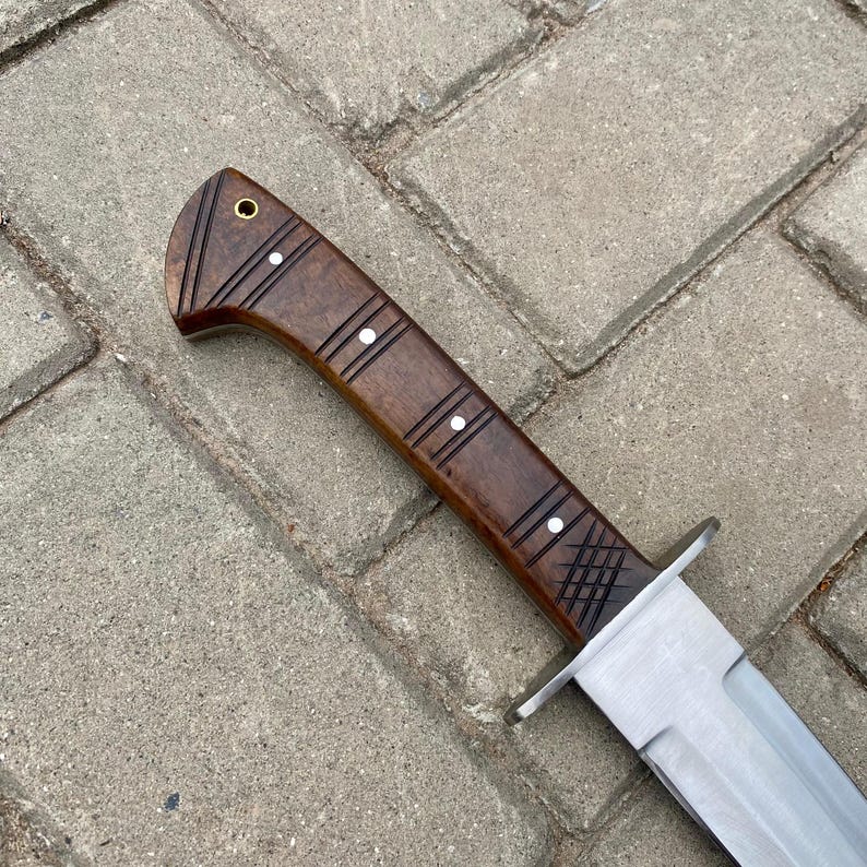 May include: A close-up of a brown wooden handle with white accents on a knife. The blade is made of stainless steel and has a sharp point.