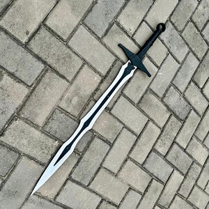 以下が含まれることがあります： 黒い柄と鍔、黒いデザインの銀色の刃を持つ長い剣。剣は灰色のレンガの表面に置かれています。剣のデザインは左右対称です。