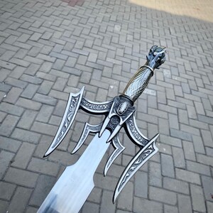 May include: A detailed, silver sword with an ornate handle and guard. The blade is wide and has a sharp edge. The handle features a dragon head design. The sword is likely made of metal.