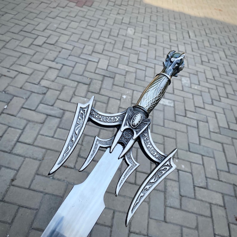 May include: A detailed, silver sword with an ornate handle and guard. The blade is wide and has a sharp edge. The handle features a dragon head design. The sword is likely made of metal.