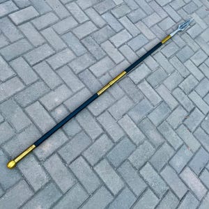 May include: A spear with a black shaft, gold accents, and a silver spearhead. The spear has a rounded gold base and a gold band near the center. The spearhead is diamond-shaped.