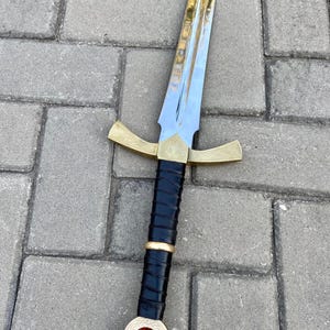 May include: A sword with a gold hilt and a red jewel on the pommel. The blade is silver and the grip is black leather.
