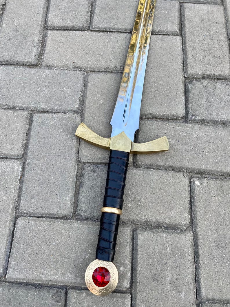 May include: A sword with a gold hilt and a red jewel on the pommel. The blade is silver and the grip is black leather.
