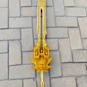 May include: A decorative sword with a silver blade and gold-colored hilt. The hilt features intricate designs and a stylized face. The sword is approximately 30 inches long.