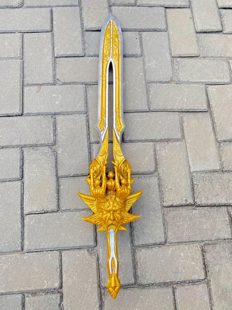 May include: A decorative sword with a silver blade and gold-colored hilt. The hilt features intricate designs and a stylized face. The sword is approximately 30 inches long.