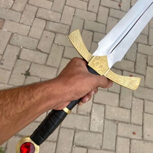 May include: A sword with a gold hilt and a red jewel at the pommel. The blade is silver and the hilt has intricate designs.