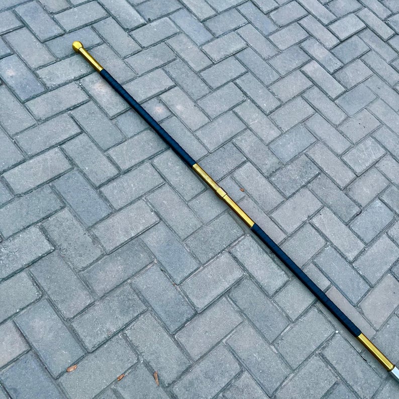 May include: A black and gold walking stick with a gold-colored tip and handle. The stick has a black center section and gold accents. The walking stick is approximately 36 inches long.