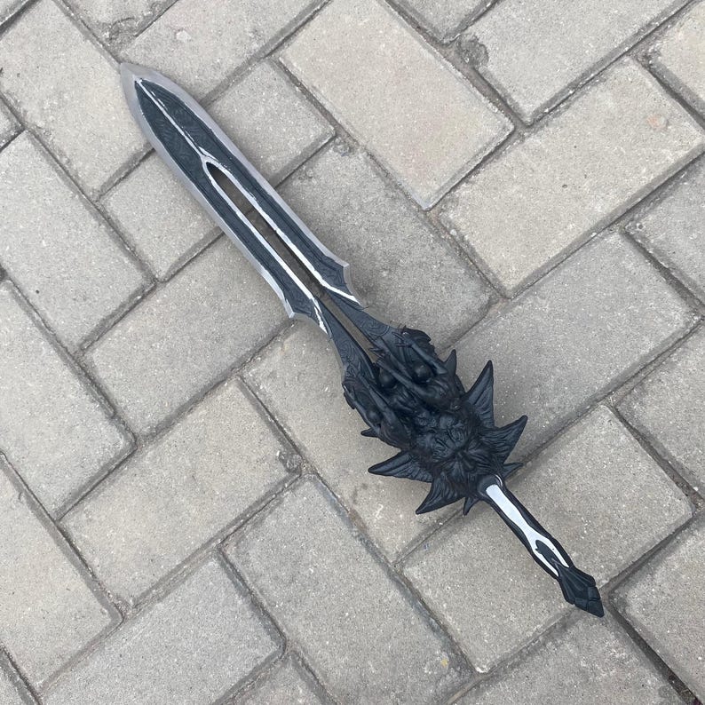 May include: A black and silver fantasy sword with intricate details. The blade has a central groove and silver accents. The hilt features a detailed dragon design. The sword is lying on a gray brick surface.