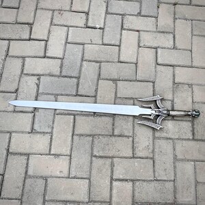 May include: A silver sword with an elaborate handle and guard, resting on a brick surface. The blade is long and straight, with a pointed tip. The handle has detailed carvings and a decorative pommel.