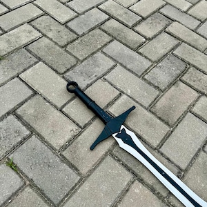 以下が含まれることがあります： 黒と白の剣。鍔とリング状の柄頭が付いています。 刃は白い中心と黒い縁があります。 剣は灰色のレンガの表面に置かれています。