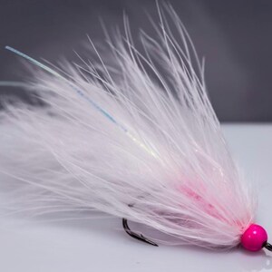 May include: A white and pink fly fishing lure with a pink bead on the end. The lure is made with feathers and has a white and blue iridescent sheen.