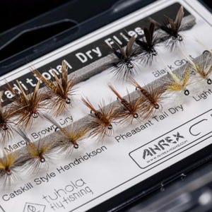 Może przedstawiać: Opakowanie tradycyjnych suchych much do wędkowania. Muchy, w tym Marc Brown Dry i Pheasant Tail Dry, są ułożone w rzędach. Haczyki mają rozmiar 12-14.