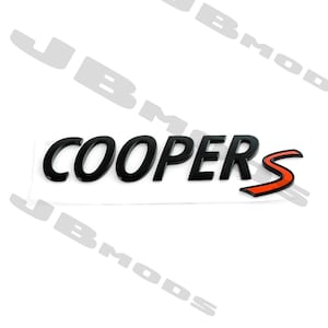 Pode incluir: Emblema preto "COOPERS S" com um acento vermelho, provavelmente para um carro Mini Cooper. As letras são em negrito e estilizadas, com um acabamento brilhante. O "S" tem uma faixa vermelha.