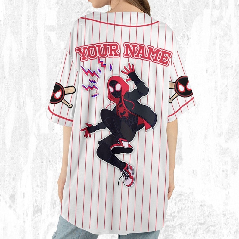 May include: White baseball jersey with red pinstripes and the text "YOUR NAME" across the back. Features a graphic of a superhero in a black and red suit. Includes baseball bat and ball graphics on the sleeves.