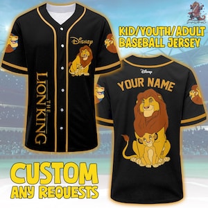 May include: Black baseball jersey featuring The Lion King characters. The jersey has gold accents, the Disney logo, and the text "THE LION KING". The back of the jersey has the text "YOUR NAME". The jersey is available in kid, youth, and adult sizes.