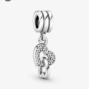 May include: A silver charm featuring two intertwined hearts. One heart is embellished with small, clear crystals. The charm has a three-ringed top for attaching to a bracelet or necklace. The design is elegant and romantic.