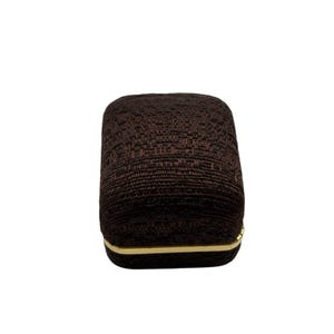 May include: A brown fabric ring box with a gold trim.